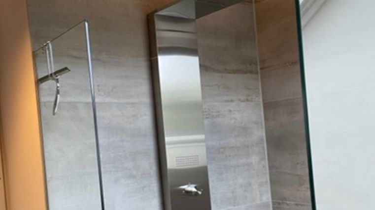 Een moderne douche met glazen afscheiding en roestvrijstalen armaturen. De wanden zijn bedekt met een eenvoudig, grijs materiaal.