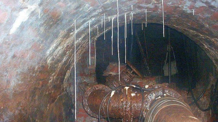 Ein Blick in einen dunklen Tunnel mit rotem Ziegelmauerwerk. An den Wänden hängen Wassertröpfchen und Rohre sind sichtbar.