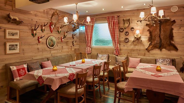 Ein gemütliches Restaurant mit Holzwänden und rustikalen Details. Die Tische sind mit karierten Tischdecken dekoriert und es hängen Geweih- und Wanddekorationen.