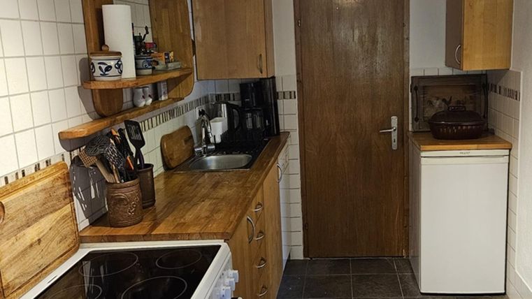 A cozy kitchen with wooden shelves and modern appliances. The walls are tiled, and there is a refrigerator next to a door.