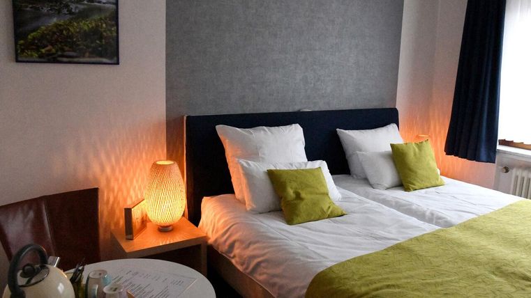 Een gezellige slaapkamer met twee eenpersoonsbedden en heldere kussens. Naast het bed staat een klein tafeltje met een waterkoker en theekopjes.