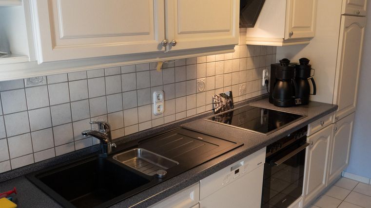 A modern kitchen with light-colored cabinets and a countertop made of dark material. The room is well-lit and contains cooking appliances as well as a sink.