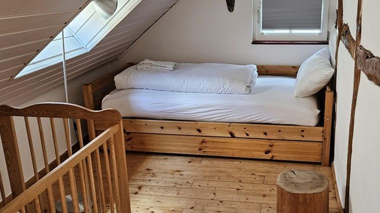 A cozy bedroom with a single bed and a children's bed. The room has hardwood floors and a bright, inviting atmosphere.