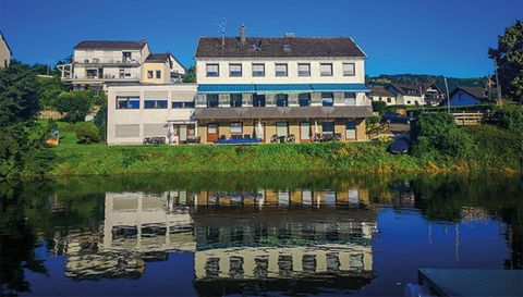 Een rustig gebouw aan het water met een duidelijke reflectie in het meer. De omgeving is groen en uitnodigend.