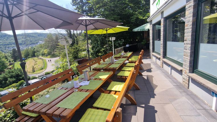 An inviting terrace with wooden tables and yellow umbrellas. In the background, green hills can be seen.