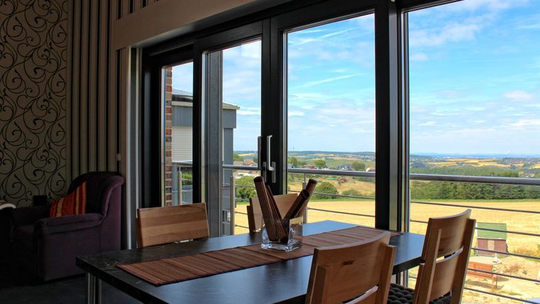 Een lichte kamer met een eettafel, stoelen en grote ramen die een prachtig uitzicht op het landschap bieden. De kamer heeft een moderne inrichting met een gezellige hoek.