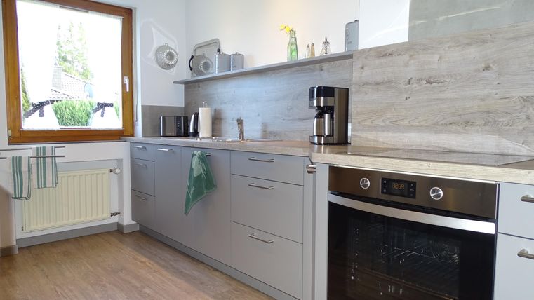 Een moderne keuken met grijze kasten en een lichte houten vloer. Een groot raam zorgt voor veel daglicht.