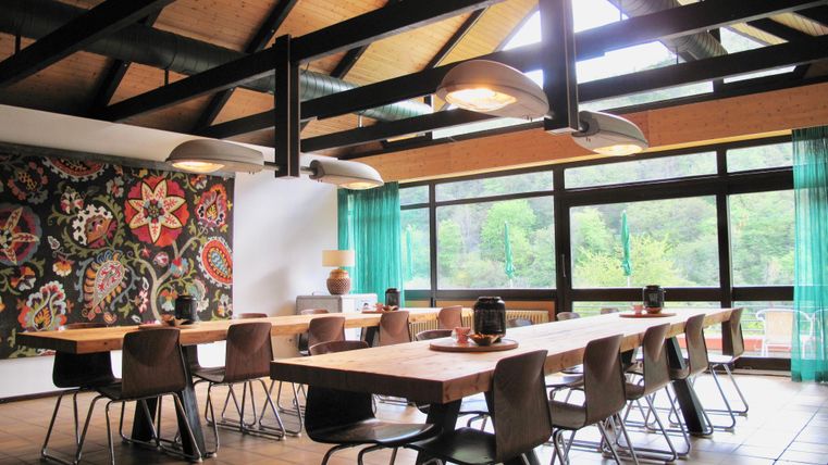 A modern room with a long table and stylish chairs. Large windows flood the space with natural light and offer a view of greenery.