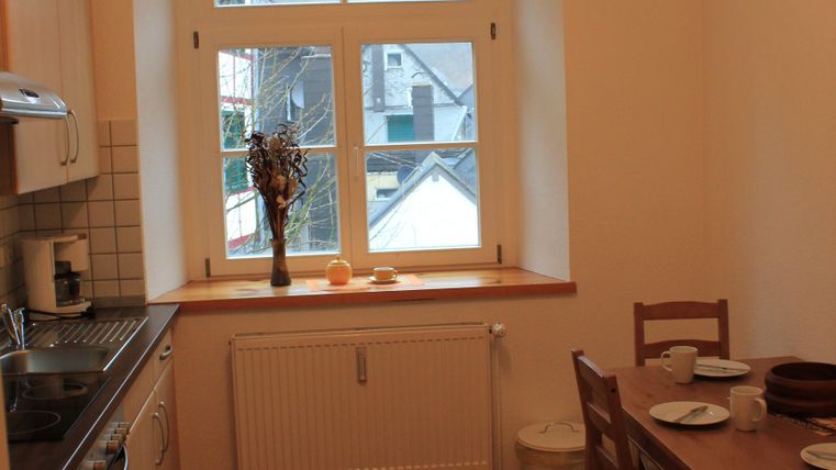 Een lichte keuken met houten vloer en grote ramen. Een tafel met servies staat naast de kooklijn.