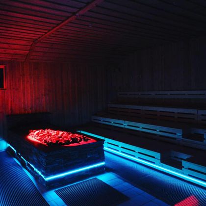 A modern sauna with colorful LED lights and rustic wooden decor. The room is cozy and invites relaxation.