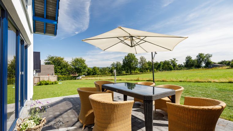 A sunny outdoor dining area with a table and chairs. In the background, a green lawn and a clear sky can be seen.