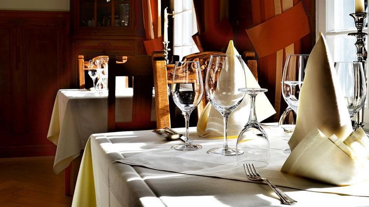 An elegantly set table in a restaurant with glasses and cloth napkins. Soft light falls through the windows, creating a cozy atmosphere.