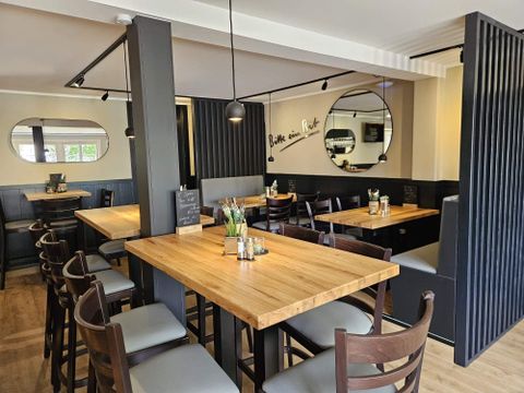 A modern restaurant with wooden tables and chairs. The walls are painted in neutral colors and reflect an inviting atmosphere.