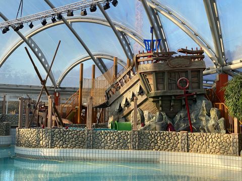 Een opwindend speelschip in een Waterpark, omringd door rotsen en planten. Het is ondergebracht in een grote, lichtovergoten hal.