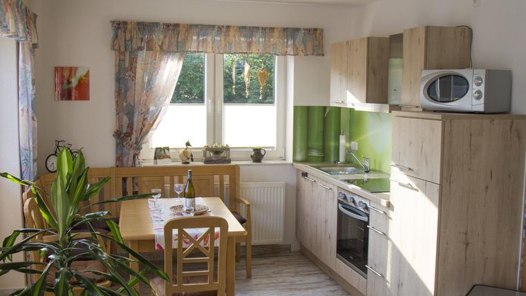 A bright kitchen with modern furniture and a large window front. The table is set for four people, and plants create a pleasant atmosphere.