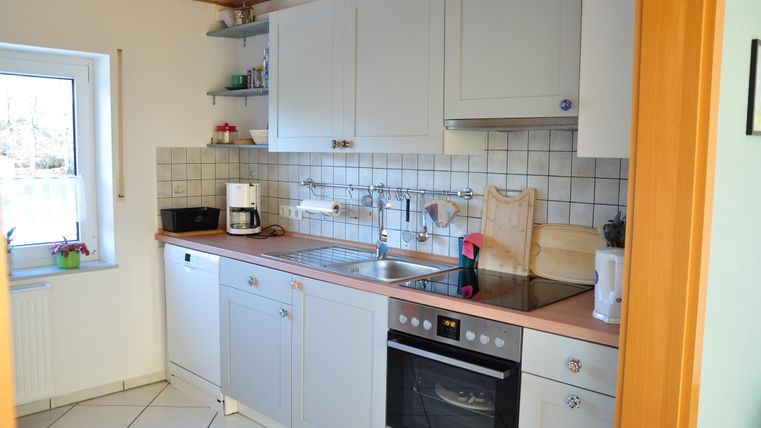 A bright, modern kitchen with white cabinets and a window that lets in daylight. The countertop is tidy and well-organized.