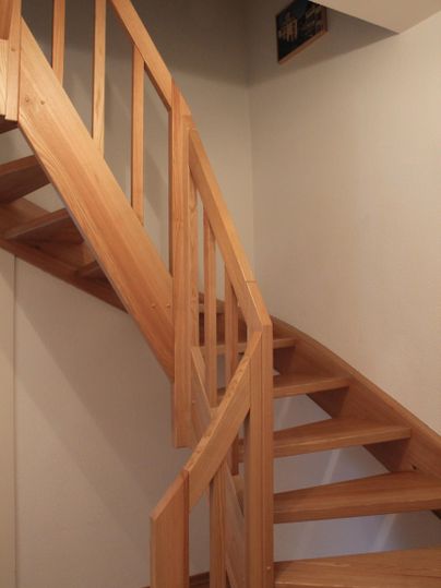 Een elegante houten trap leidt naar boven. De muren zijn eenvoudig en in lichte kleuren gehouden.