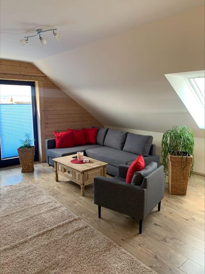 A cozy living room with a gray sofa and red cushions. The room has large windows and a small table in the center.
