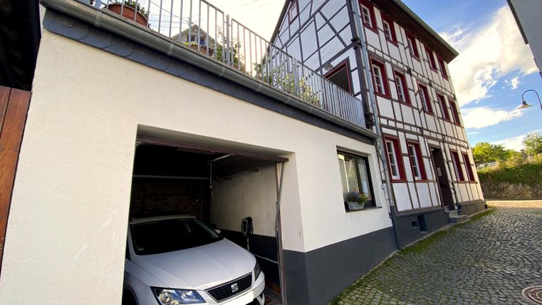 Een modern huis met vakwerkarchitectuur en een garagegebied. In de garage staat een witte auto.