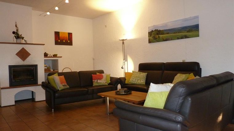 A modern living room with black leather sofas and a wooden coffee table. The walls are light, and there are artworks as well as a fireplace.