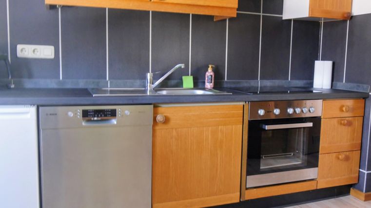 A modern kitchen with wooden cabinets and stainless steel appliances. The area is tidy and well-organized, featuring a stove, a sink, and a dishwasher.