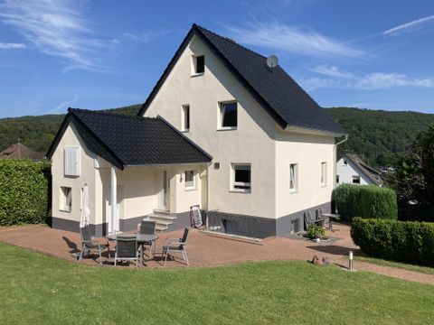 A modern, bright house with a black roof and an inviting terrace. The garden is well-maintained and the landscape is green.