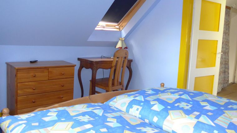 A cozy bedroom with a bed, a dresser, and a desk. The walls are light blue, and a yellow door adds a splash of color.
