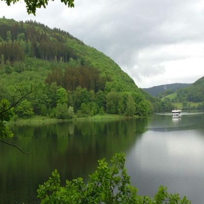 A tranquil lake surrounded by green hills and trees. In the background, a small boat can be seen.