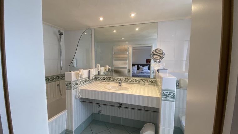 A modern bathroom with a large mirror and a bright, friendly atmosphere. The walls are tiled, and there is a shower as well as a bathtub.