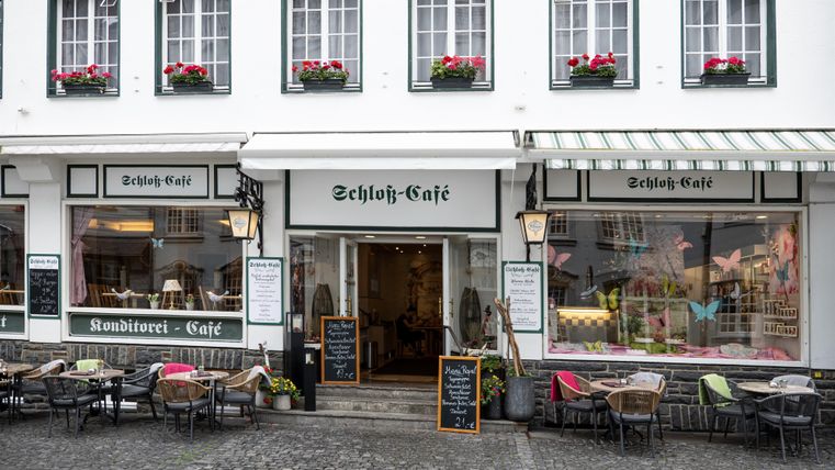 Ein charmantes Café mit Außenplätzen und Blumenarrangements. Die Fassade ist traditionell und einladend gestaltet.