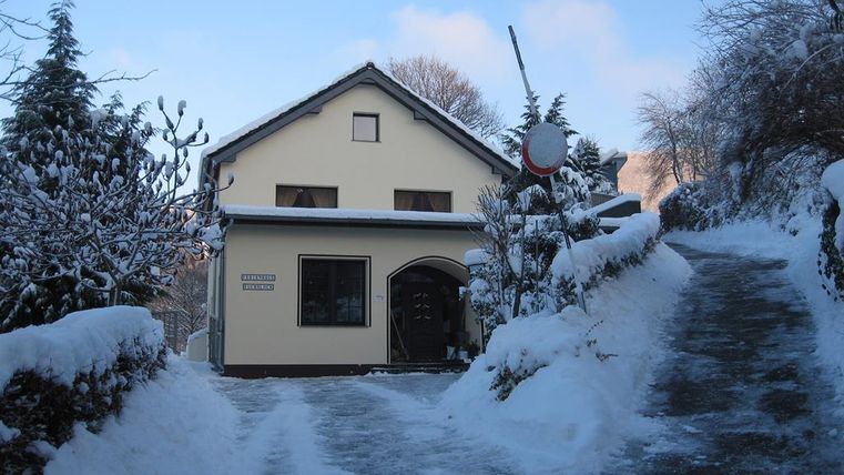 A charming house in winter covered with snow. The path to the house is also covered with snow and lined with trees.