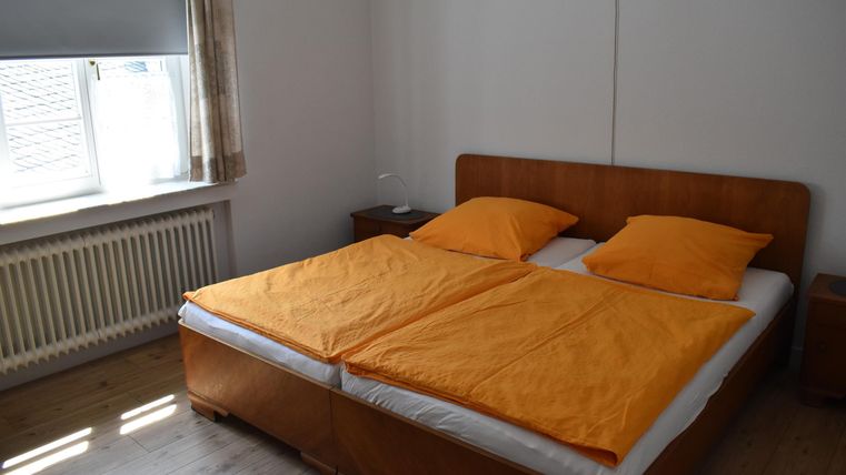 Ein schlichtes Schlafzimmer mit einem großen Doppelbett und orangefarbenen Bettdecken. Das Zimmer hat ein Fenster, das Tageslicht hereinlässt.