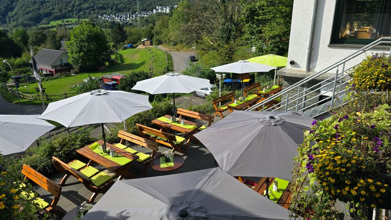 A cozy outdoor area with wooden tables and sun umbrellas. The view of the green landscape is relaxing and inviting.