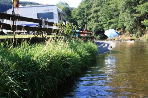 Een campingplaats in een groene omgeving met veel bomen. Verschillende campers en tenten zijn zichtbaar tussen de natuur.