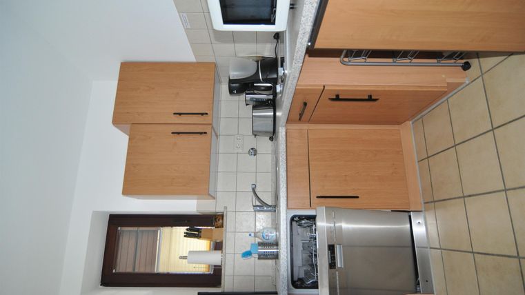 A modern kitchen with wooden cabinets and bright tiles. There is a stove, a sink, and modern kitchen appliances.
