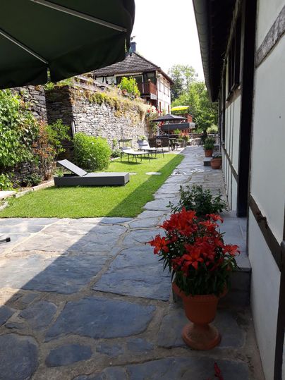 Een mooie tuin met een verzorgd gazon en bloeiende rode bloemen. Op de achtergrond zijn gezellige zitplekken en een modern huis te zien.