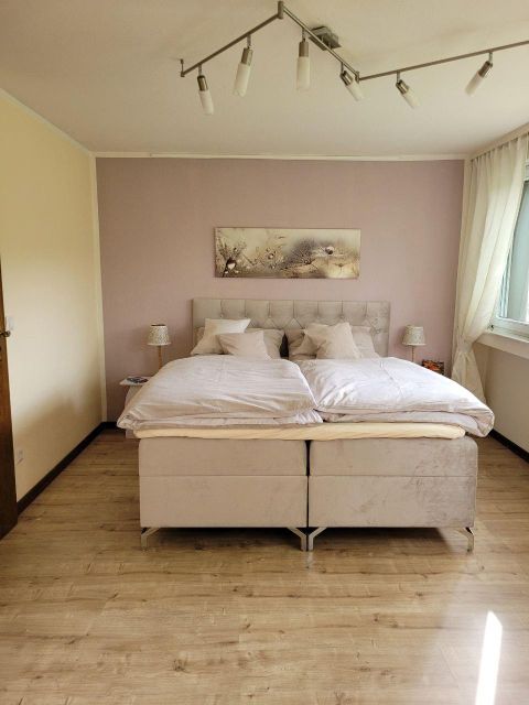 Ein modernes Schlafzimmer mit einem großen Doppelbett und sanften Farben. Das Zimmer hat einen helle Atmosphäre durch das Tageslicht und einige Dekorationen.