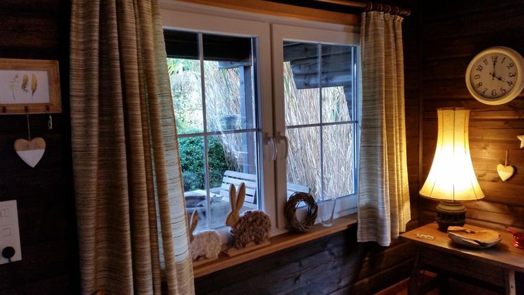 A cozy room with a window through which one can see a garden. Next to the window stands a lamp, and there are other decorative elements visible.
