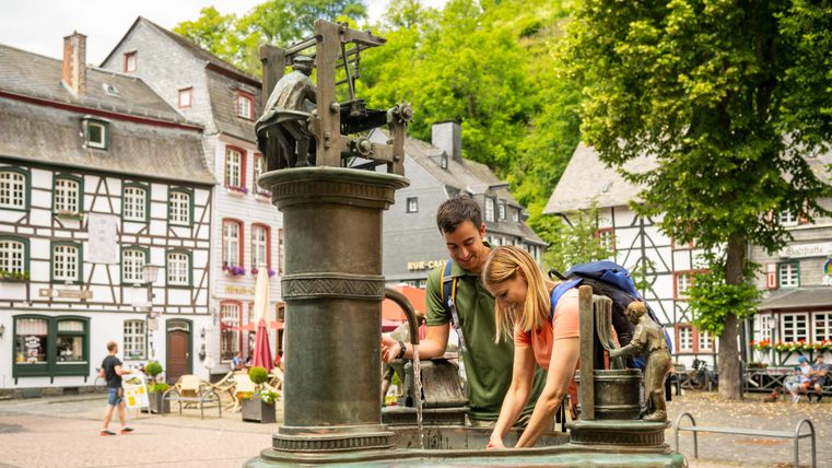 Ein schöner Platz mit einem Brunnen und alten Fachwerkhäusern. Ein Paar steht am Brunnen und schaut hinein.