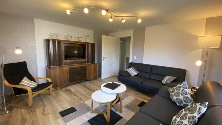 Een moderne woonkamer met een gezellige bank, een televisie en een stijlvolle tafel. Het ruimteontwerp is licht en uitnodigend, met een houten vloer en aangename verlichting.