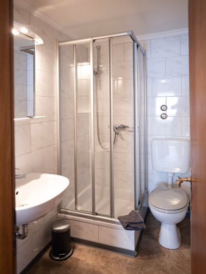 A modern bathroom with a shower, a sink, and a toilet. The walls are covered with light tiles.