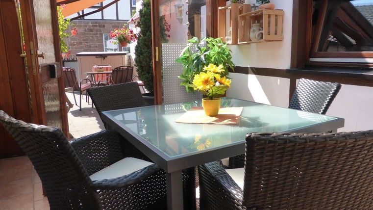 Een gezellige binnenplaats met een glazen tafel en mooie stoelen. Op de tafel staat een bloeiende pot met zonnige bloemen.