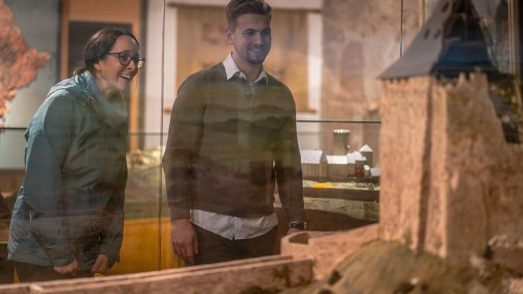 Twee bezoekers kijken geïnteresseerd naar een model van een kasteel in een museum. De twee lijken enthousiast over de tentoonstelling.