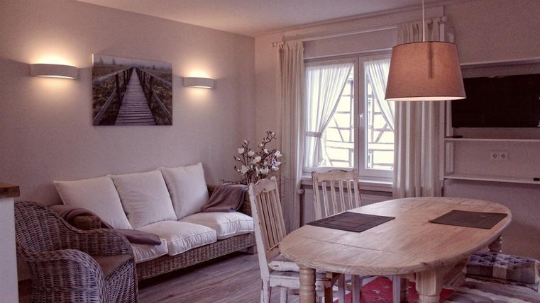 Een gezellige woon- en eetkamer met een ronde houten tafel en stoelen. De ruimte is helder en vriendelijk, met een bank en natuurlijk licht door grote ramen.
