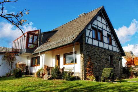 Een gezellig huis met een mix van moderne en traditionele elementen. Het is omgeven door een verzorgde tuin en heeft een duidelijke blauwe lucht op de achtergrond.