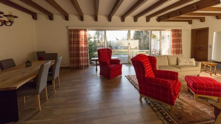 A bright living space with a wooden beam ceiling. Red armchairs and a large dining table characterize the cozy atmosphere.