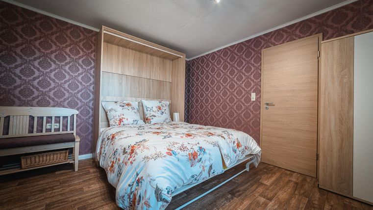 Een gezellige slaapkamer met een tweepersoonsbed en een houten wandafwerking. De muren zijn versierd met een elegant patroon, en er is ook een kribbetje in de kamer aanwezig.