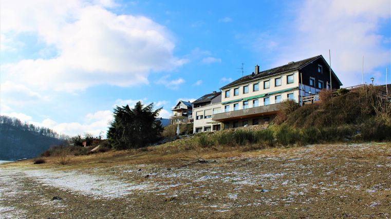 A house on the slope with a view of a clear sky and some clouds. The ground is dry and has a natural environment.