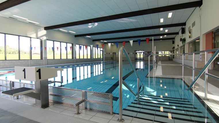 Ein modernes Hallenbad mit klarem Wasser und großen Fenstern. Die Treppe führt zum Schwimmbecken, das gut beleuchtet ist.