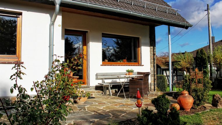 Een modern huis met een uitnodigende entree. Voor de voordeur staan een tuinstoel en potten, omringd door planten.